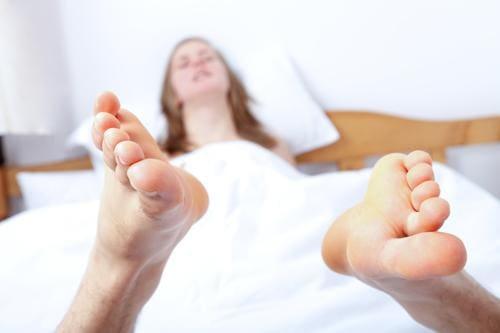 Close-up of unshaven feet of a person lying in bed covered with white sheets