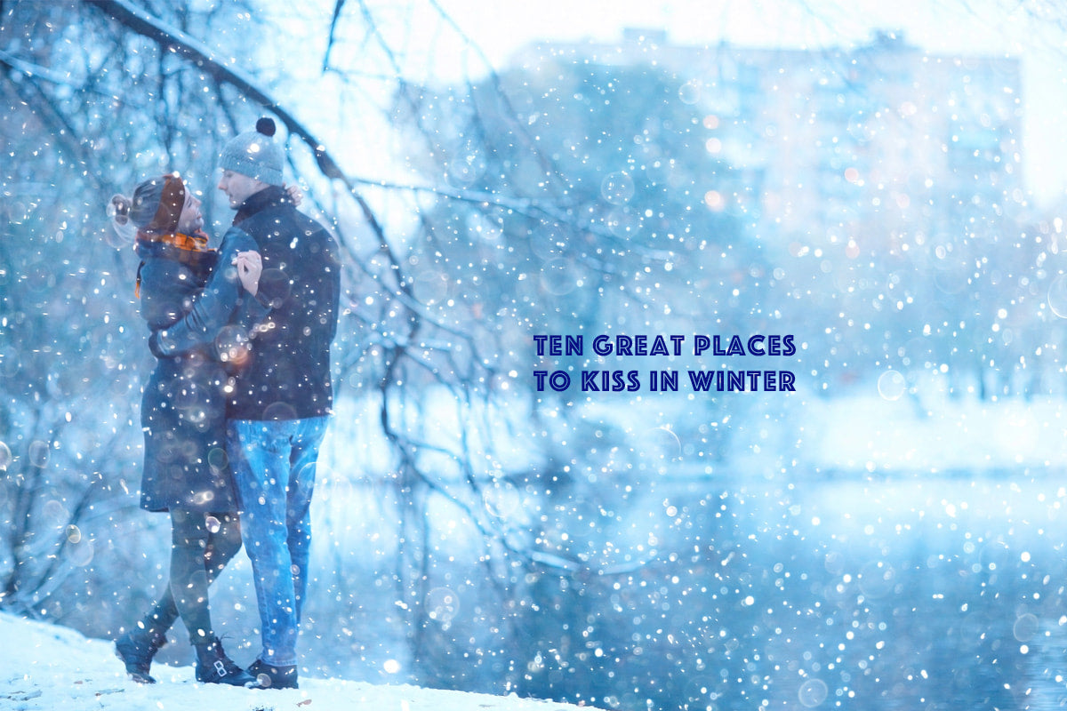 Couple embracing in snowy winter park with falling snow and cityscape background