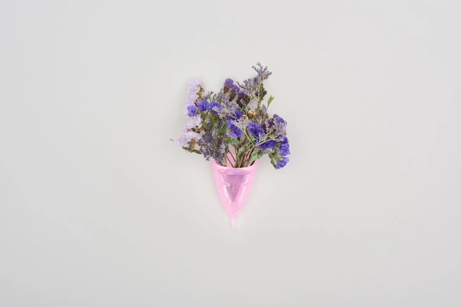 Pink menstrual cup holding purple and lavender wildflowers on white background
