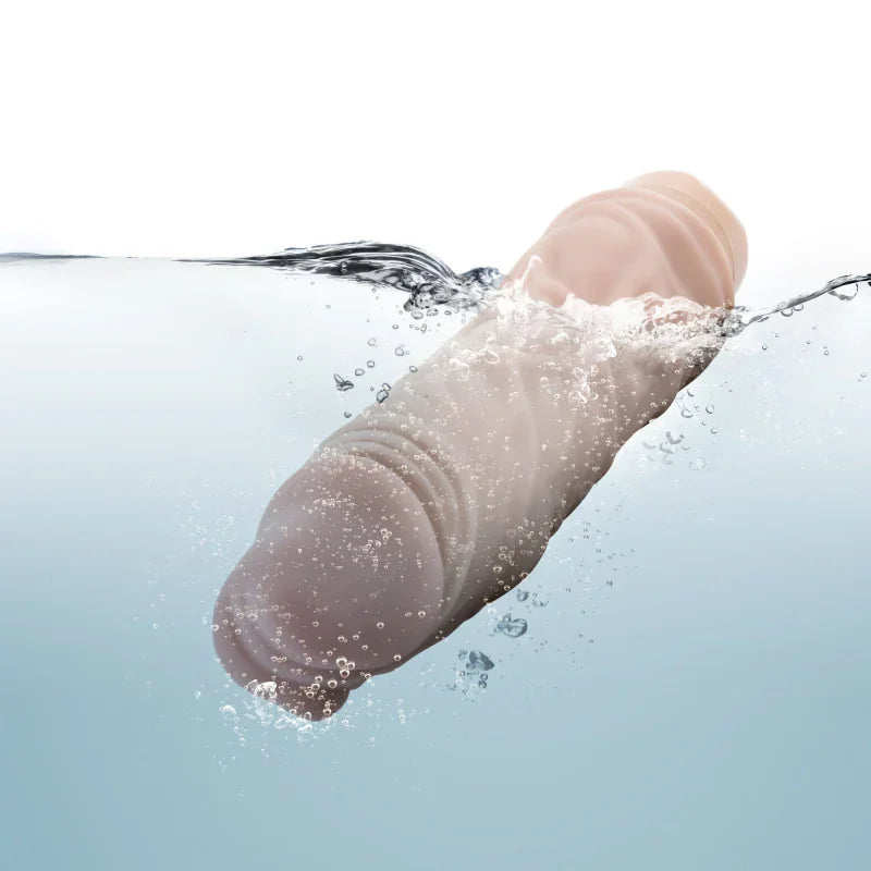 Natural-colored realistic silicone cock vibrator submerged in water with bubbles, waterproof adult toy