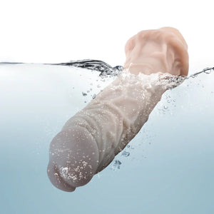 Realistic skin-toned silicone vibrator partially submerged in water with bubbles