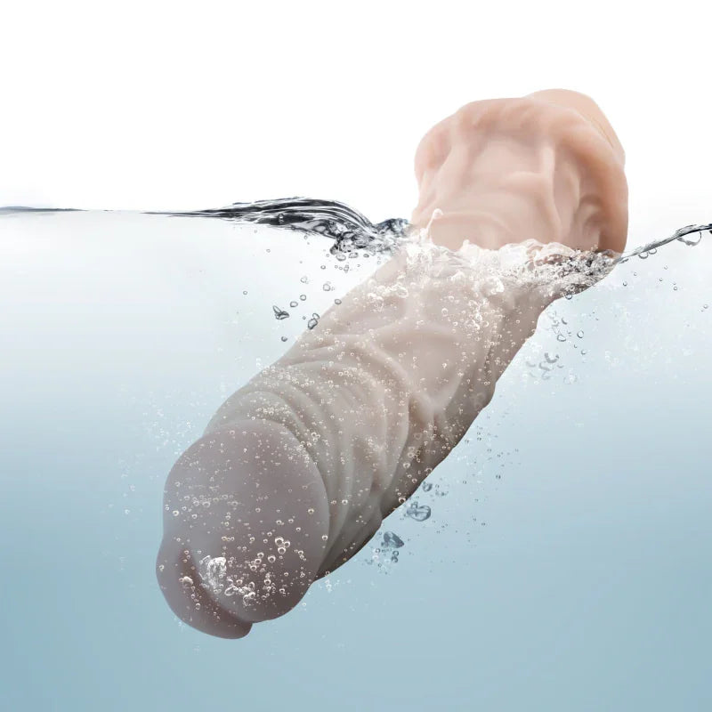 Realistic skin-toned silicone vibrator partially submerged in water with bubbles